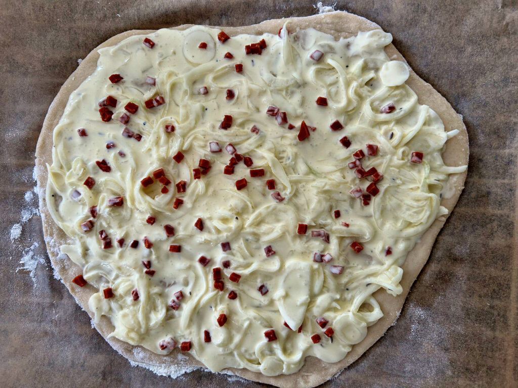 Ziebel-Schmandcreme mit Speck auf dem Teig verteilen