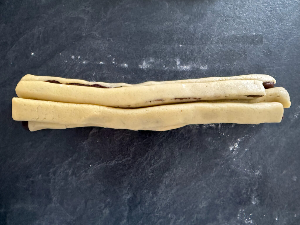 Den hellen Teig ausrollen und wieder um die Würstchen wickeln